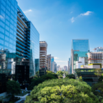 Centro corporativo moderno espelhado com árvores sob céu azul ensolarado.