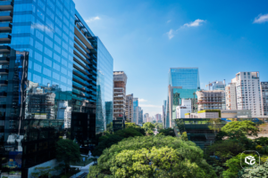 Centro corporativo moderno espelhado com árvores sob céu azul ensolarado.